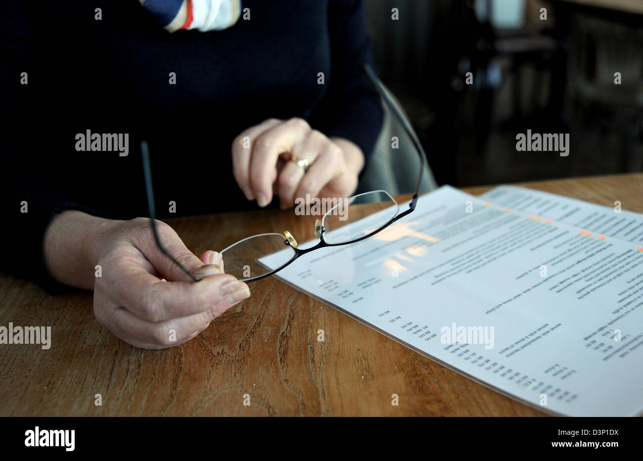 Donna che tiene in mano un paio di occhiali a tavola per leggere un menu Foto Stock