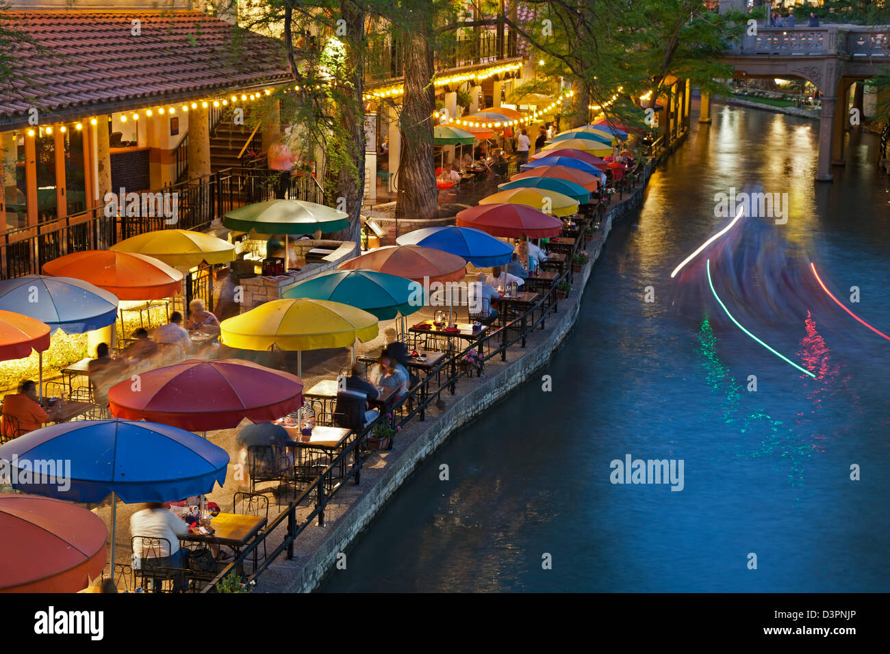 Ombrelloni colorati, barca striature chiare sul fiume San Antonio e il lungofiume di San Antonio, Texas, Stati Uniti d'America Foto Stock