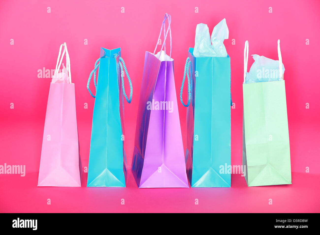 Gruppo di colorati negozi di sacchetti di carta in piedi sul pavimento rosa isolato su sfondo rosa Foto Stock