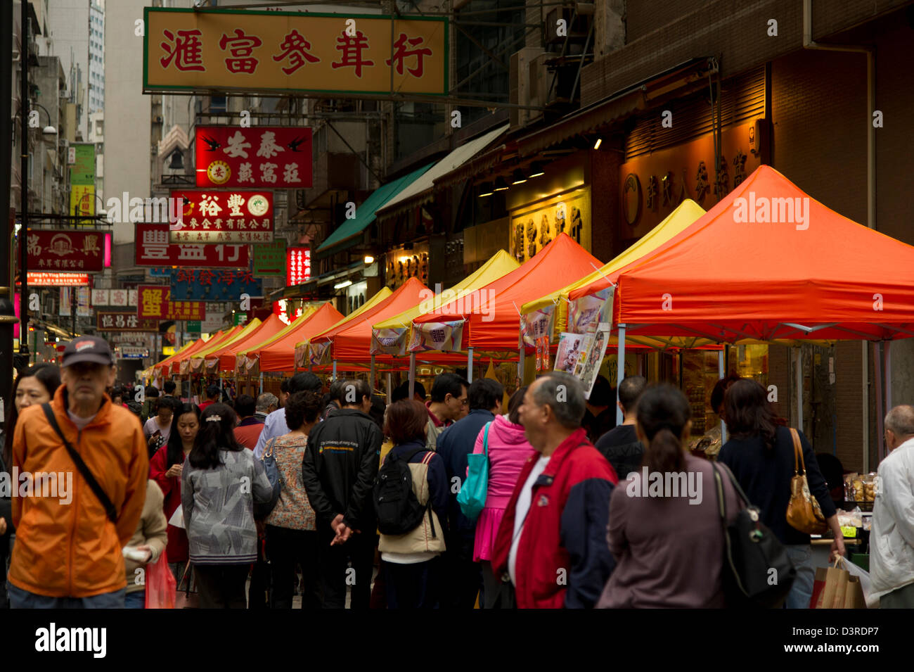 Shoppers folla passato arancione e giallo tende a comparsa in un Hong Kong street al crepuscolo Foto Stock