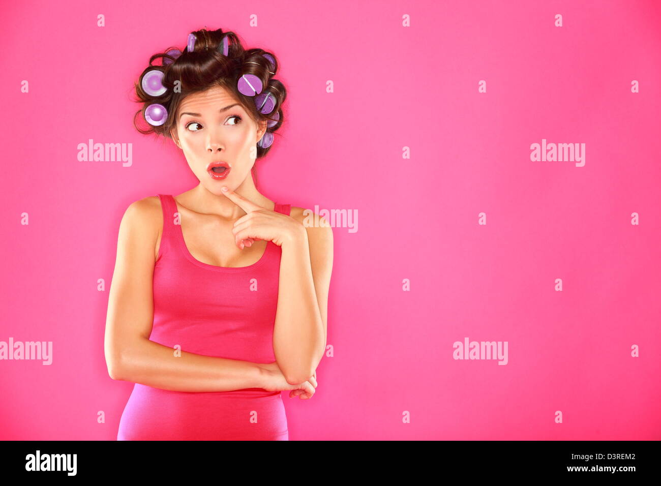 Bella pensieroso funky giovane donna con i capelli rulli guardando al lato piedi isolato su sfondo rosa Foto Stock