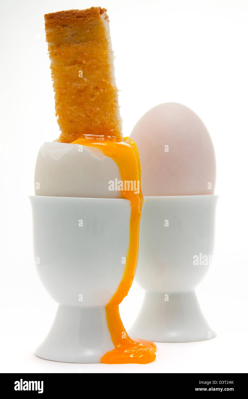 Uova sode con un soldato tostato in un uovo cup con un gocciolamento vibrante tuorlo d'uovo Foto Stock