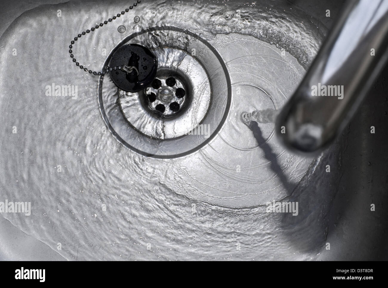 L'acqua corrente che scorre lungo il plughole in un lavello da cucina in acciaio inox Foto Stock