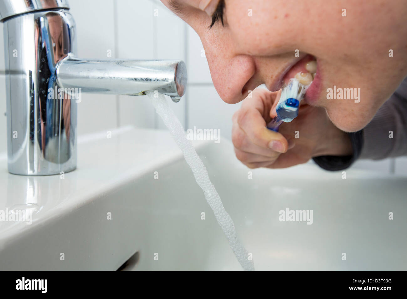 La donna sta spazzolando i suoi denti, mentre l'acqua è ancora in esecuzione dal rubinetto. Immagine simbolo per lo spreco di acqua. Foto Stock