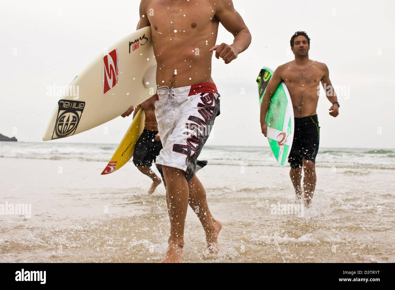 Surfers in esecuzione in mare a freddo, Sant Agnese, Cornwall, Regno Unito Foto Stock