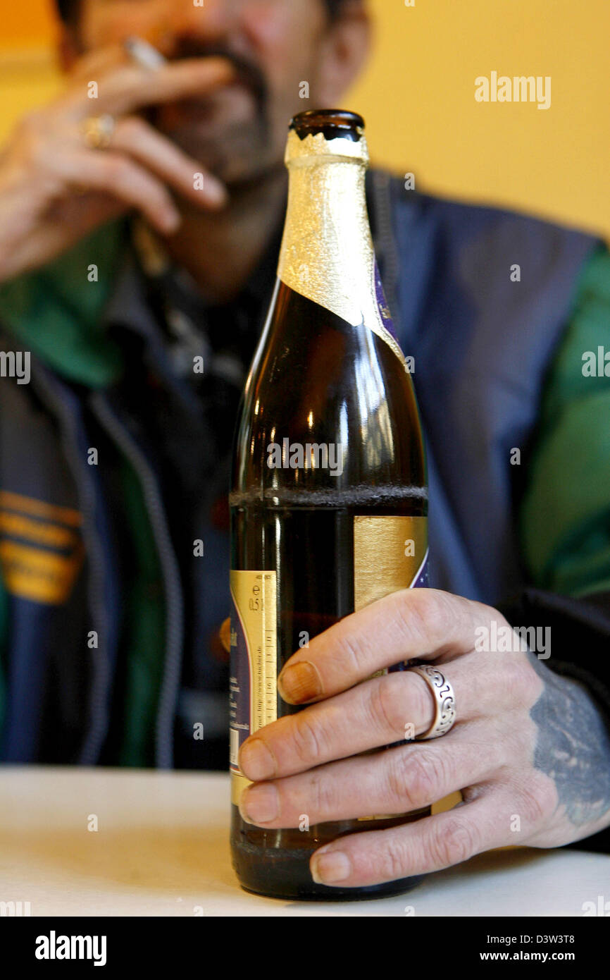 Il venditore di un senzatetto giornale" contiene una bottiglia di birra nella mano sinistra e prende un trascinamento da una sigaretta nella sua mano destra in Nuremberg, Germania, giovedì, 14 dicembre 2006. Foto: Daniel Karmann Foto Stock
