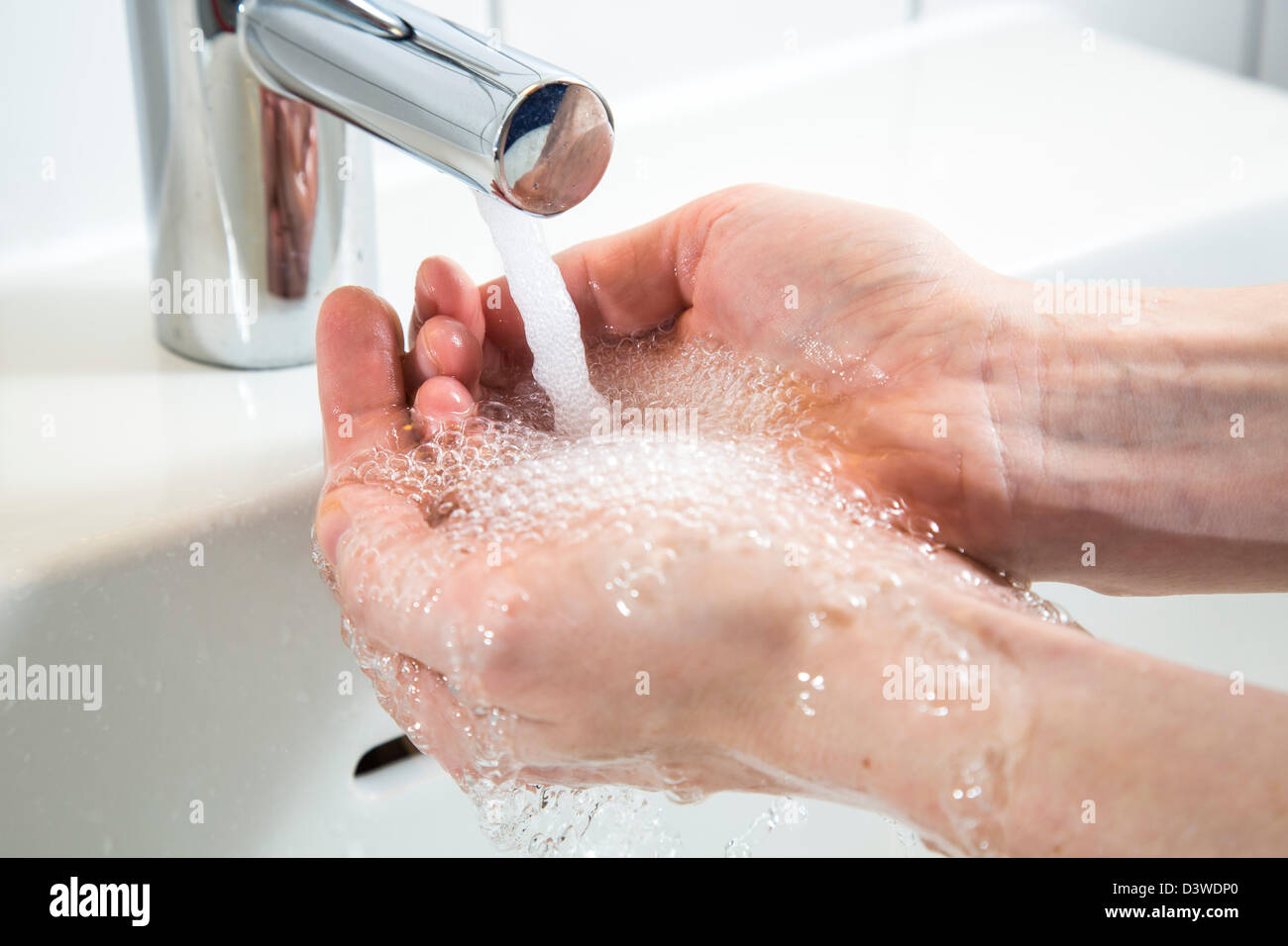 Persona sta lavando le mani sotto l'acqua da un rubinetto in un bagno. Immagine simbolo per lo spreco di acqua. Foto Stock