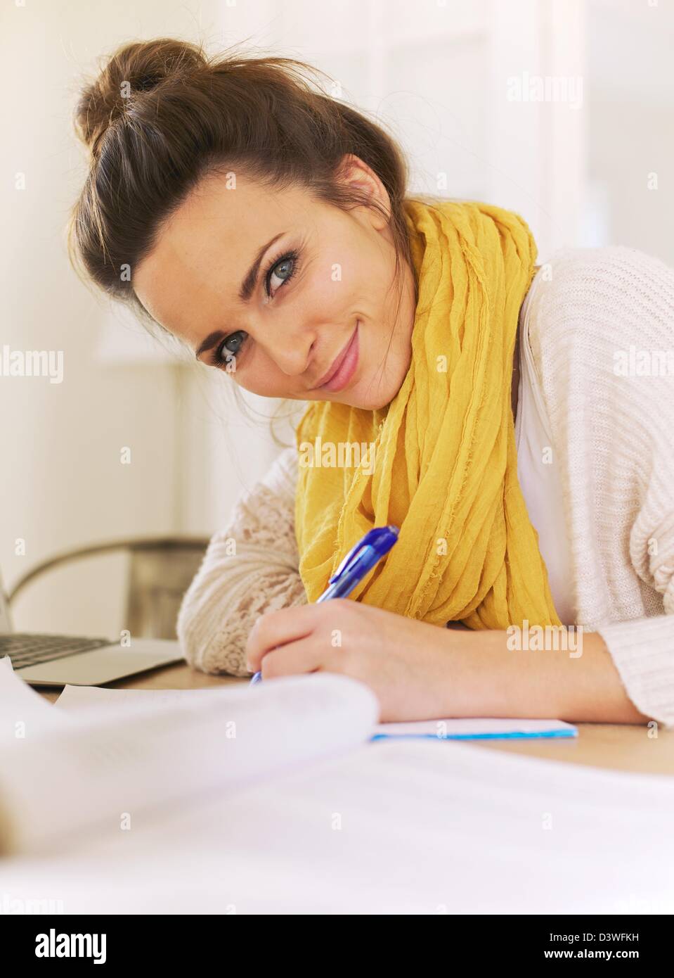 Primo piano di una bella donna sorridente guardando la fotocamera durante la scrittura sul suo blocco note Foto Stock
