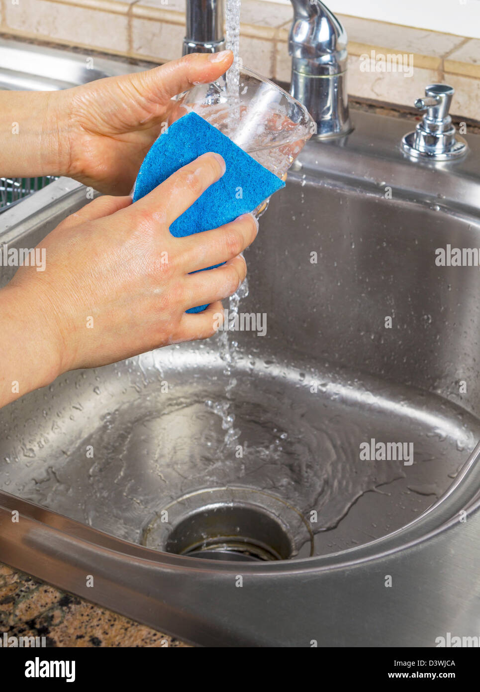 Foto verticale di femmine della pulizia delle mani un bicchiere con acqua che scorre dal rubinetto di cucina lavandino Foto Stock
