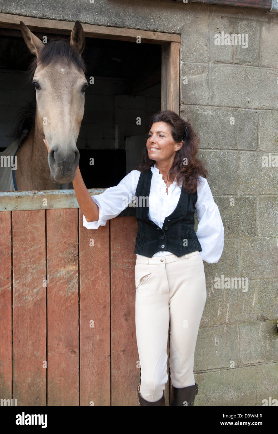 Una donna matura felicemente pacche un cavallo in un Cotswold cantiere stabile Foto Stock