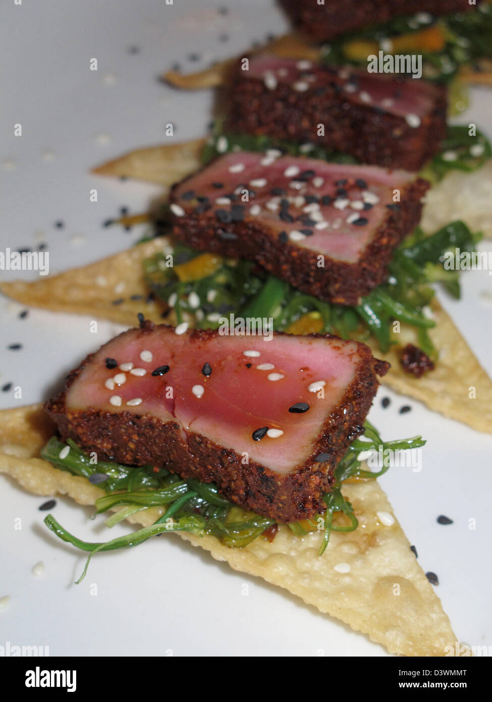 Prodotti alimentari - di sesamo e quasi in crosta rosolata Ahi Tonno piatto. Semi di sesamo tonno coperto dei tranci di pesce sul cracker e verdi. Foto Stock