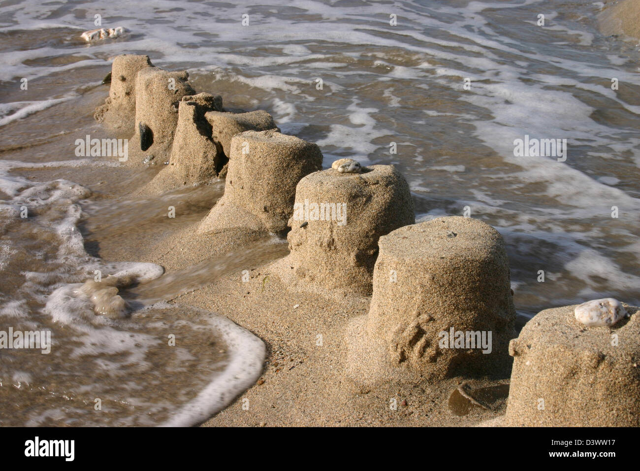 Le rovine di un castello di sabbia di essere spazzati via dal mare Foto Stock