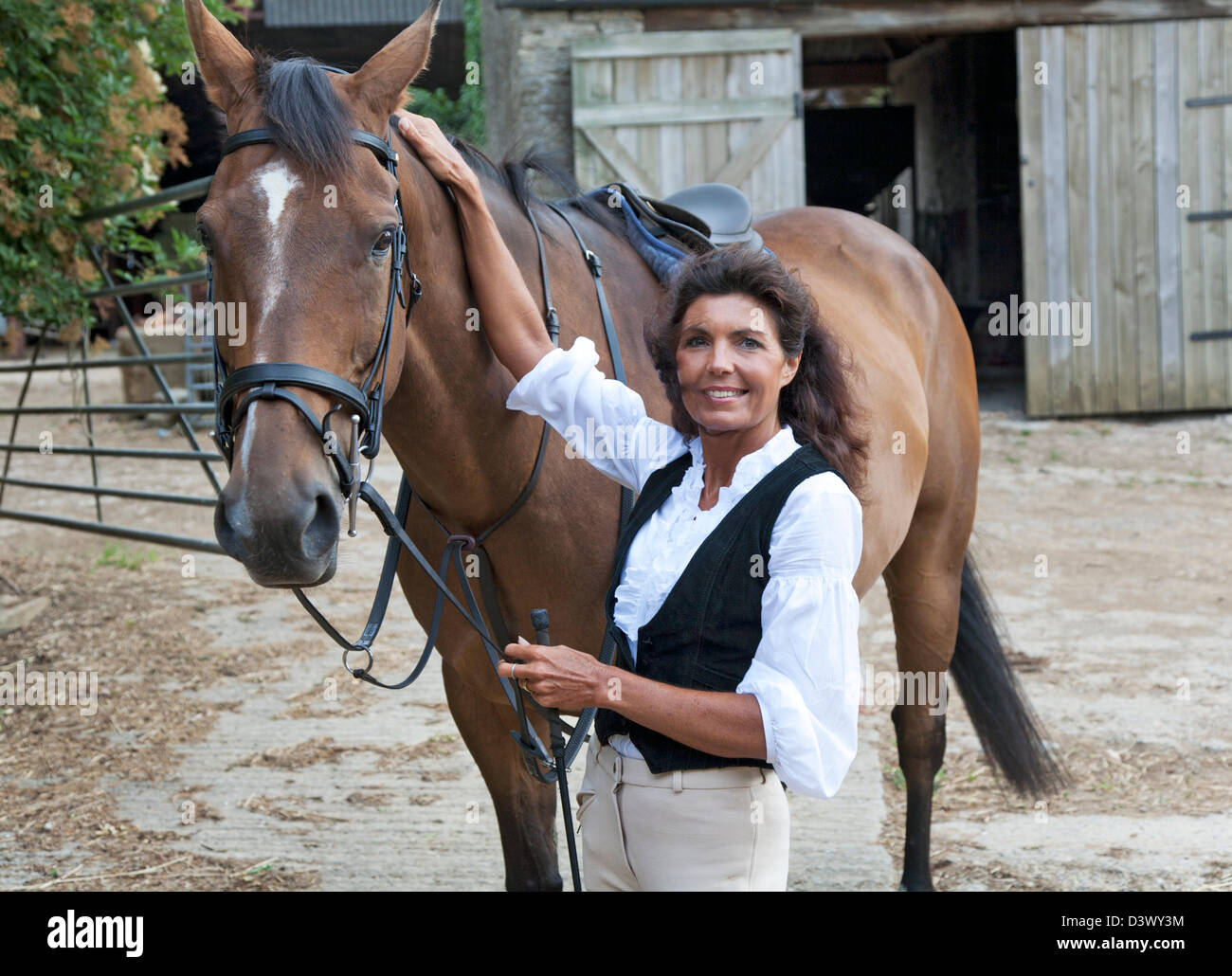Una donna matura con il suo grande cavallo in un Cotswold cantiere stabile Foto Stock
