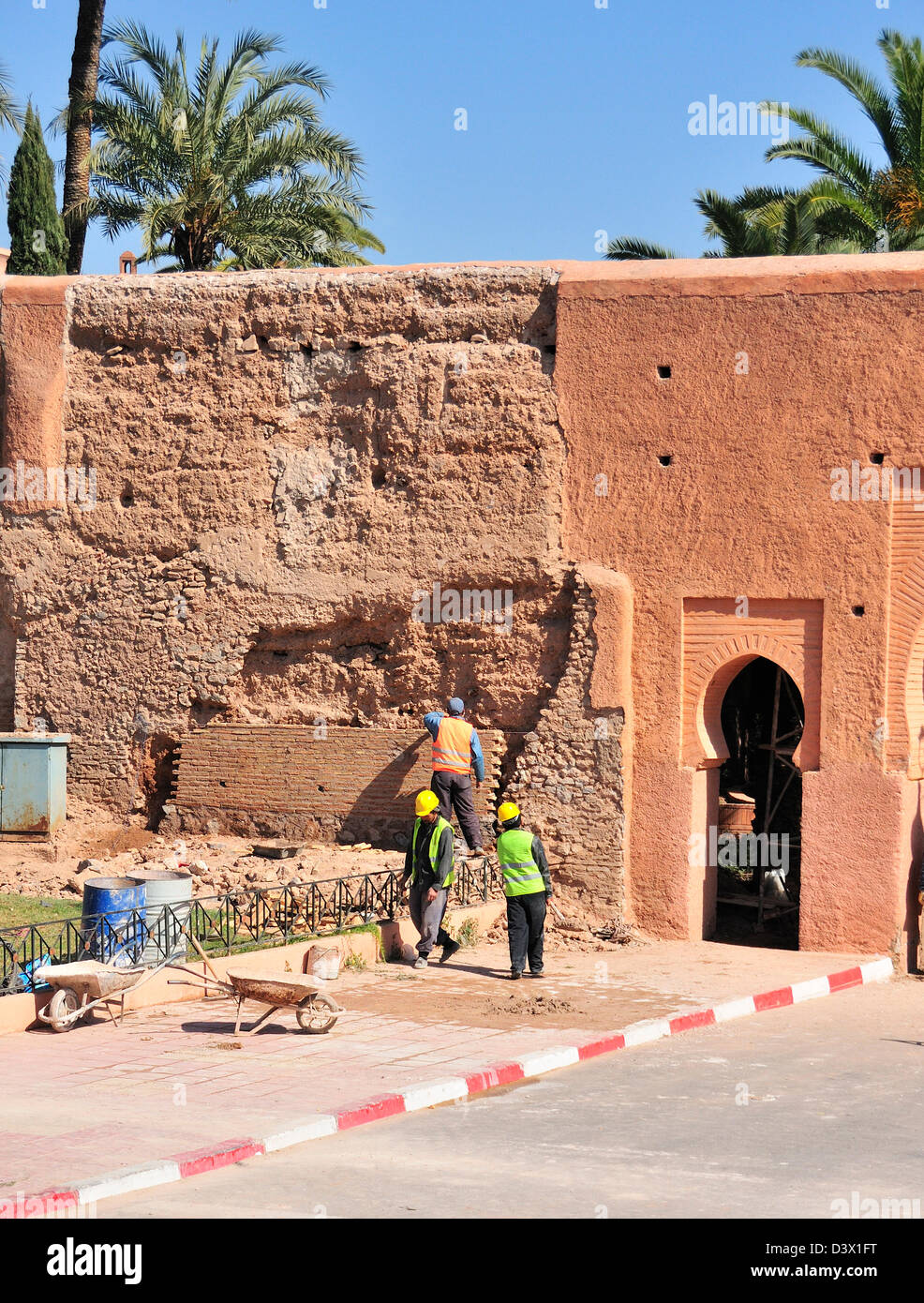 Operai che effettuano riparazioni al pavimento di fronte alle vecchie mura di mattoni di fango rosa-rossastro di Marrakech, Marocco, Africa del Nord Foto Stock