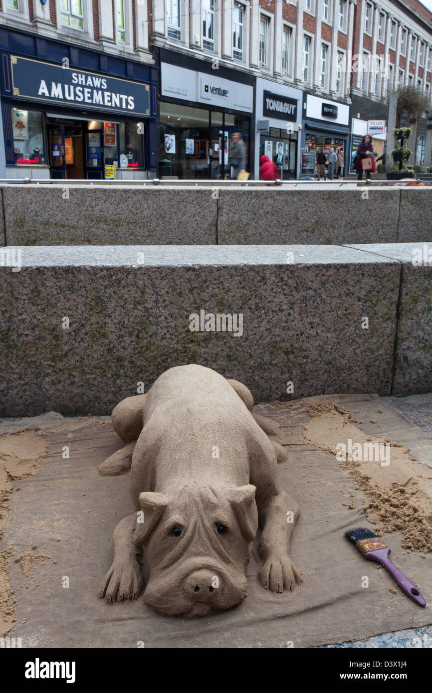 La scultura di sabbia di un cane sdraiato sul marciapiede  le strade e i negozi della città di Warrington borough nella zona di Cheshire, Inghilterra, Regno Unito Foto Stock