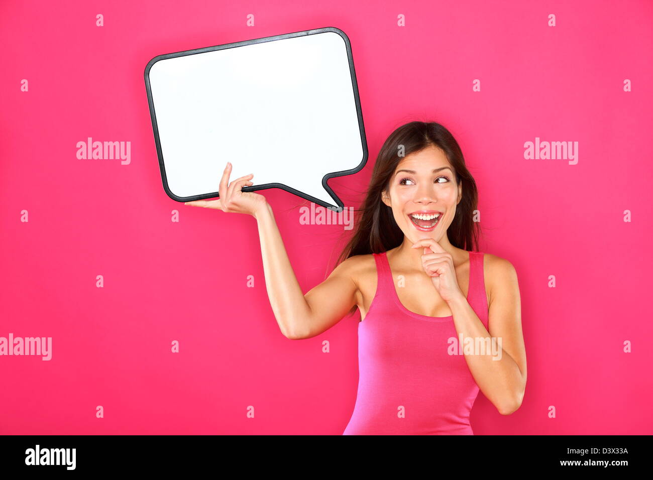Bella felice multirazziale caucasico / Cinese asiatica giovane donna che mostra vuoto discorso bolla banner isolato su sfondo rosa Foto Stock