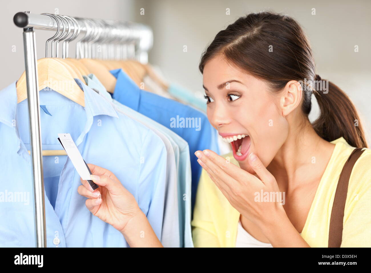 Felice razza mista cinese Asiatica / Caucasian giovane donna sorpreso al di sopra dei prezzi di vendita guardando il cartellino del prezzo su vestiti in negozio Foto Stock