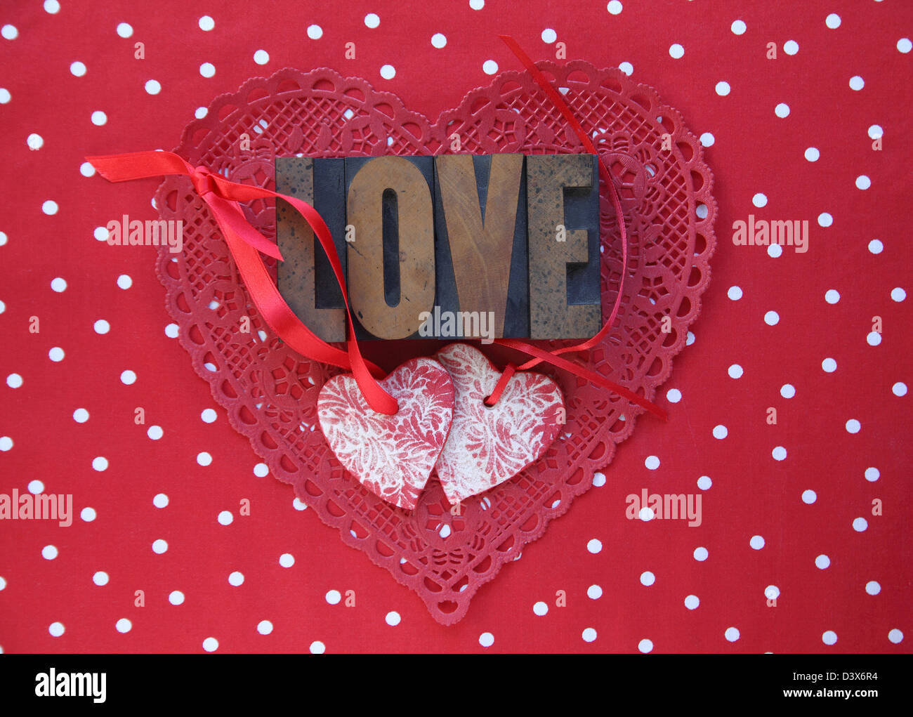 La parola "amore" con ornamenti di cuore e di nastri di colore rosso su rosso e bianco polka dot sfondo Foto Stock