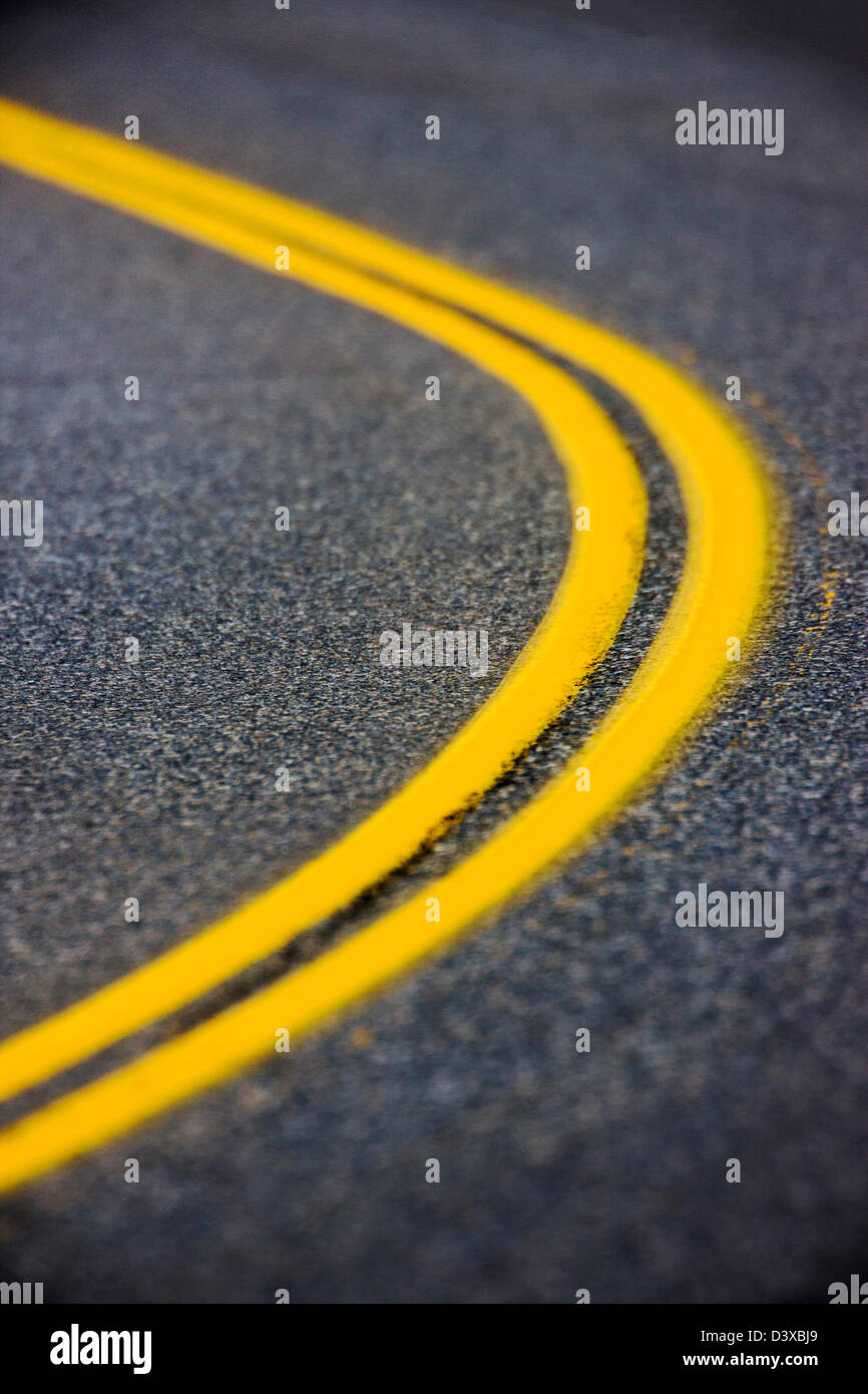 Un teleobiettivo fotografia della parte curva a doppia linea gialla su una strada asfaltata Foto Stock