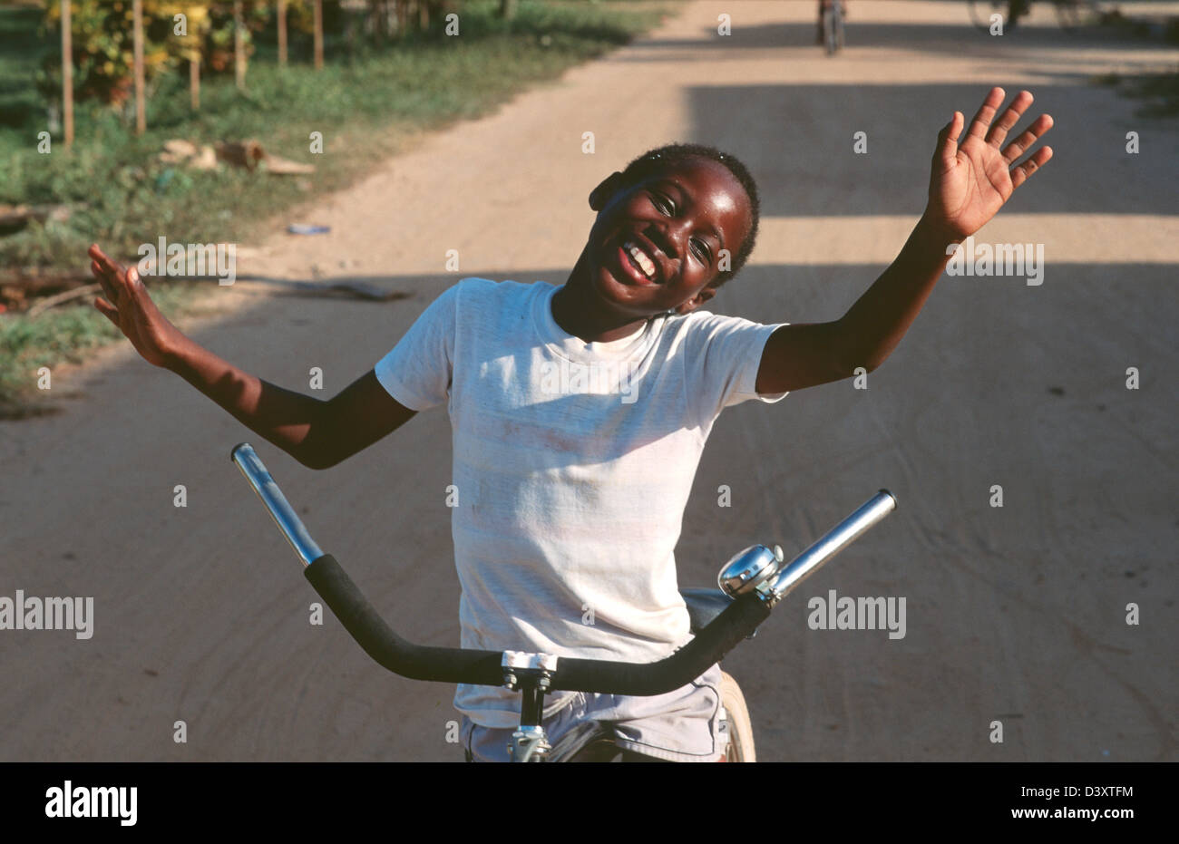 Ragazzo felice, sulla sua bicicletta, le braccia si stese dicendo Ciao, Dangriga, Belize Foto Stock