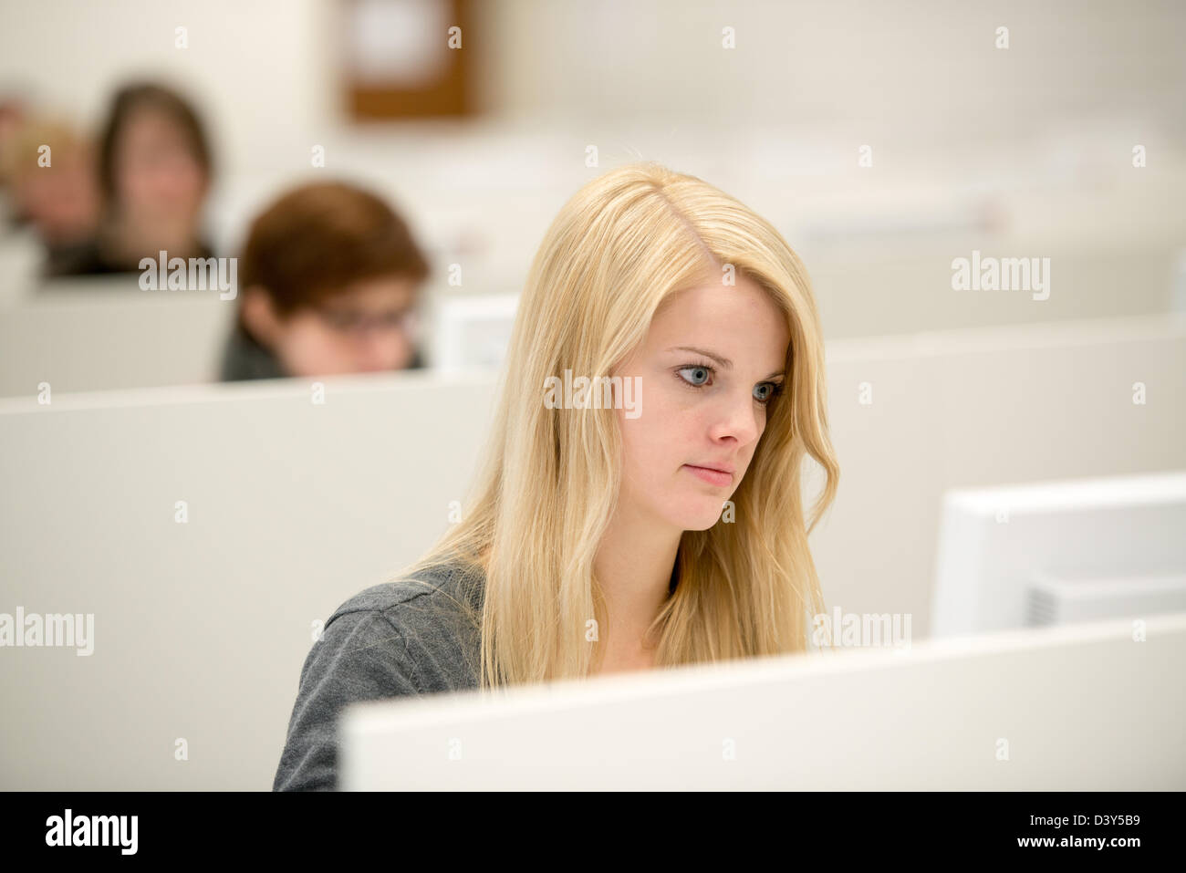 Yound ragazza bionda funziona con computer desktop, sullo sfondo di altre ragazze che lavorano Foto Stock