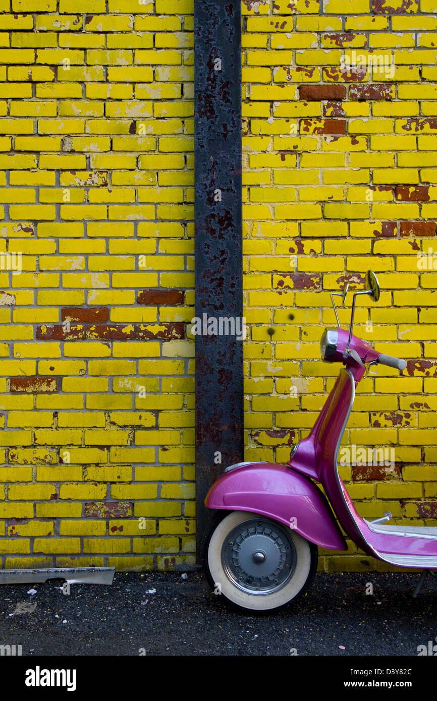 Un colorato di rosa scooter contro un mattone giallo parete. Foto Stock