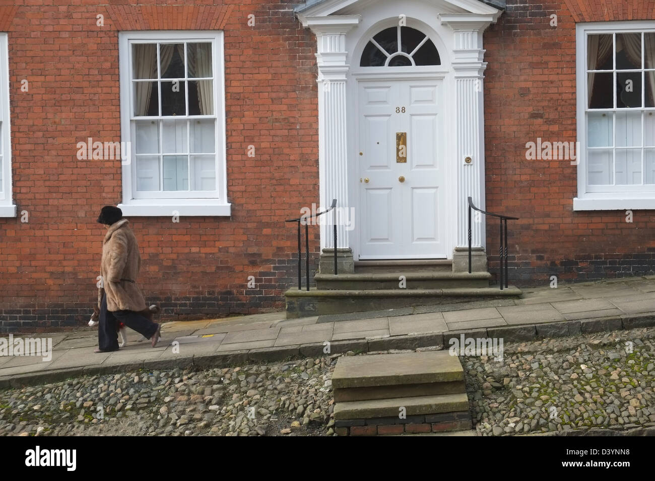 Donna in pelliccia e hat passeggiate passato Georgian House no.38 in Broad Street, Ludlow, Shropshire, Inghilterra, Gran Bretagna Foto Stock