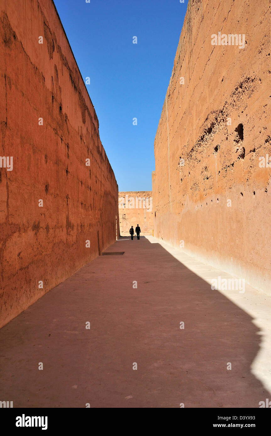 Matura in lontananza camminando tra due antiche tinte di rosa alte mura a El Badii Palace, Marrakech, Marocco Foto Stock
