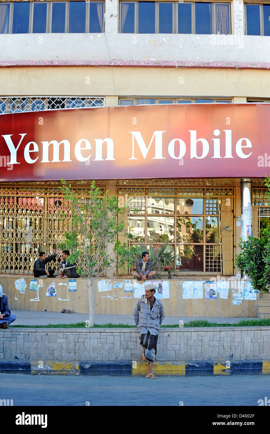 Poveramente vestito uomo seduto fuori da un telefono Mobile shop a Sana'a, Yemen. Foto Stock