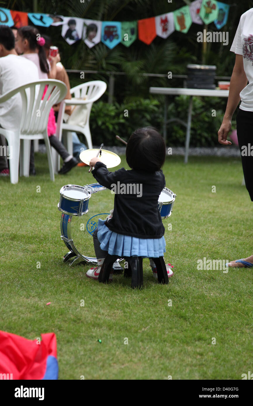 Si tratta di una foto di una bambina che sta suonando la batteria o la batteria in un giardino durante una parte. Essa è vista dal retro. Foto Stock