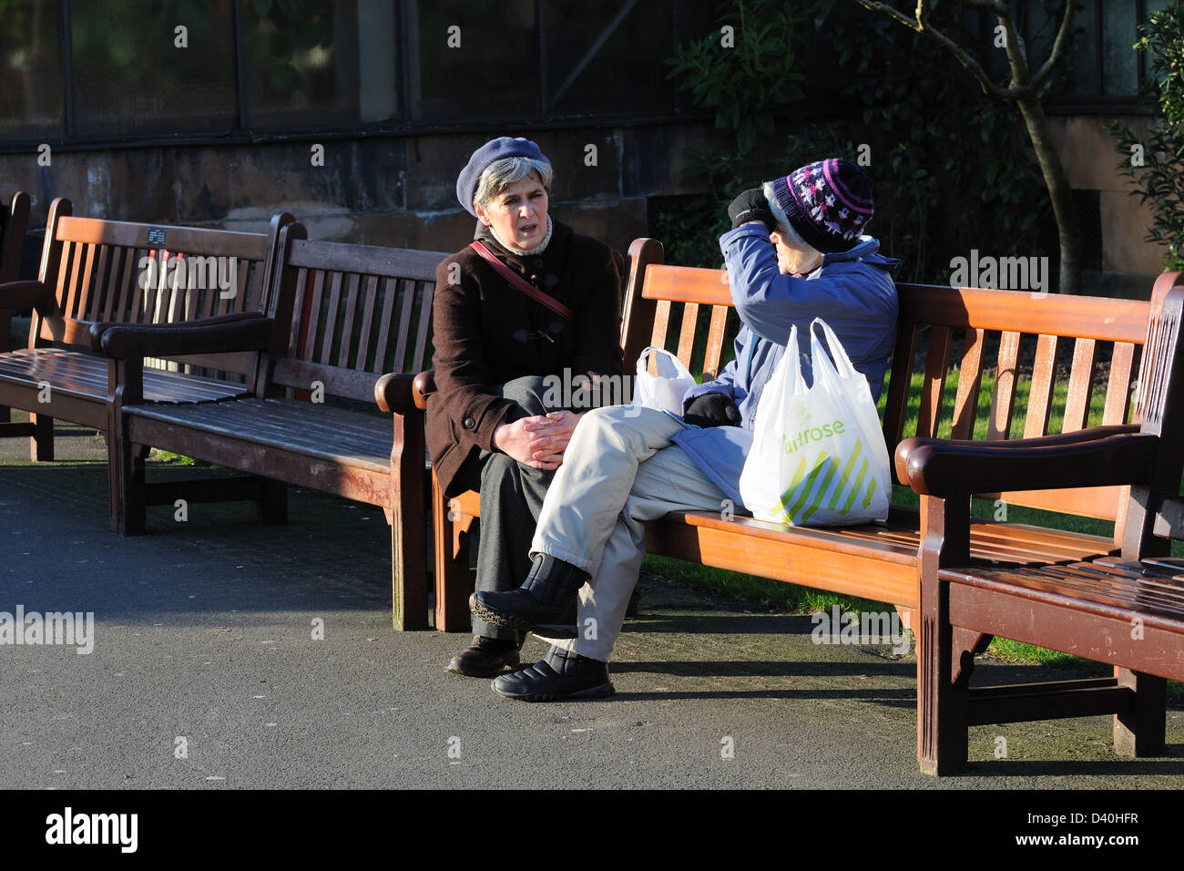 Due donne prendono una pausa dallo shopping di sedersi a parlare in un parco locale, Glasgow, Scotland, Regno Unito Foto Stock