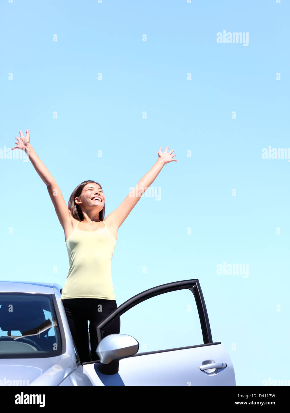 Giovane e bella multirazziale Asian / Caucasian donna con braccia alzate di uscire di nuovo auto sotto il cielo blu Foto Stock
