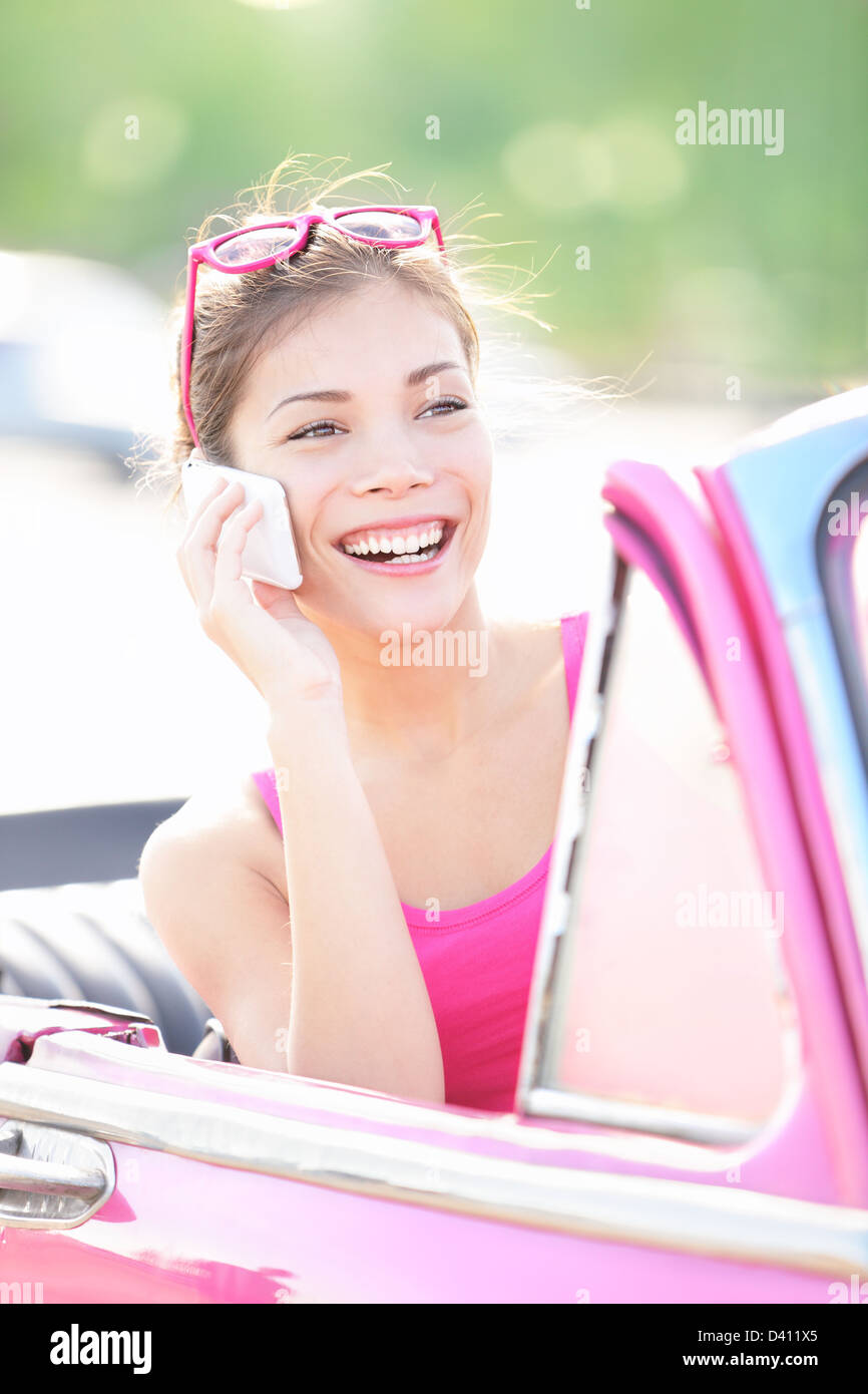Giovane e bella sorridente razza mista donna in rosa auto retrò parlando su smart phone Foto Stock