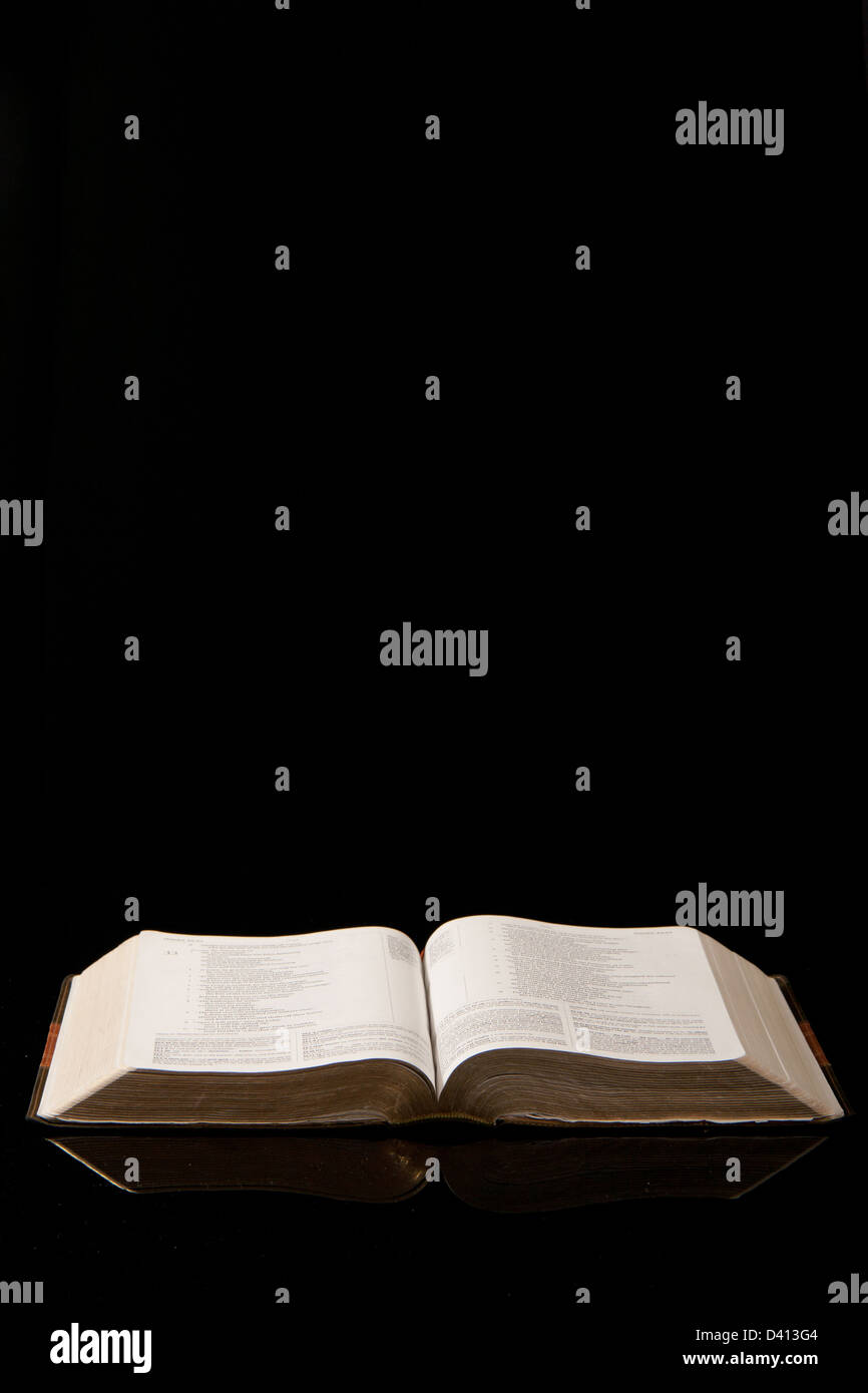 Un aprire la Bibbia insieme contro uno sfondo nero. Foto Stock