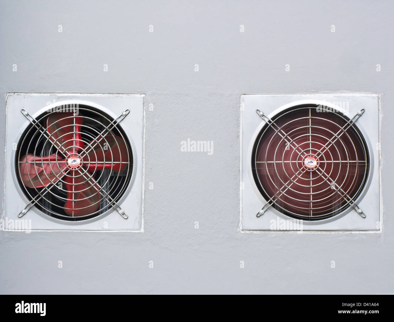 Una coppia di rosso ventilato industriale ventola sul muro grigio come sfondo Foto Stock