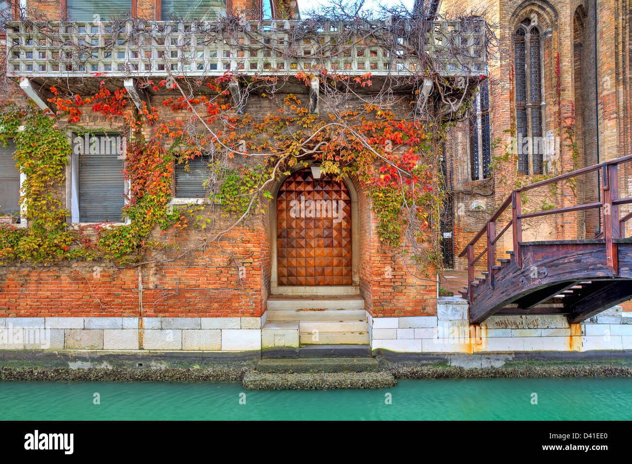 Vite copre la facciata della casa in mattoni rossi accanto a stretto canale e il piccolo ponte di legno a Venezia, Italia. Foto Stock