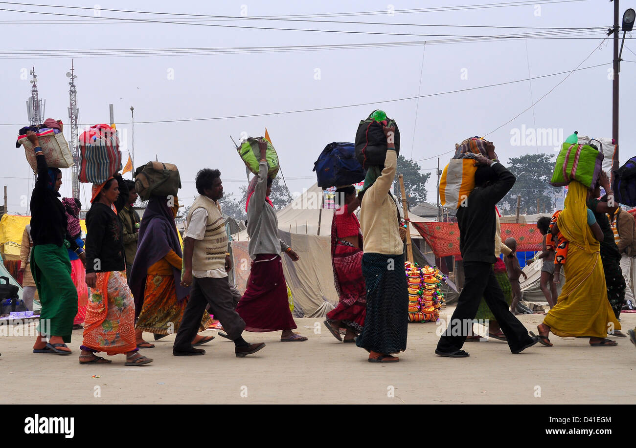 Devoti Hindu portano i loro averi sulle loro teste come lasciano il Kumbh Mela in Allahabad Foto Stock