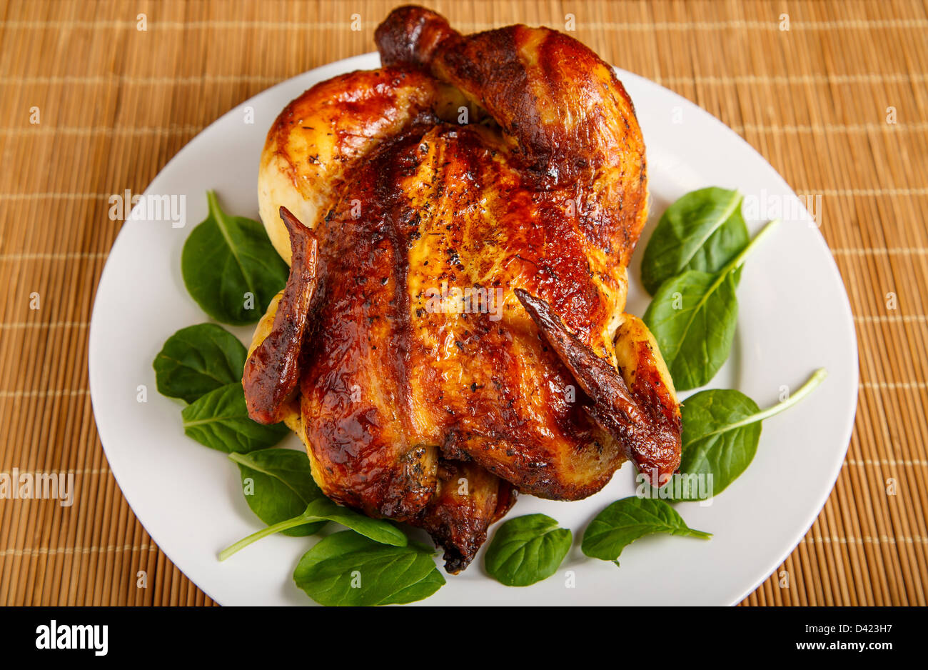 Un intero pollo arrosto su una piastra bianca e bambù placemat guarnita con baby spinaci Foto Stock