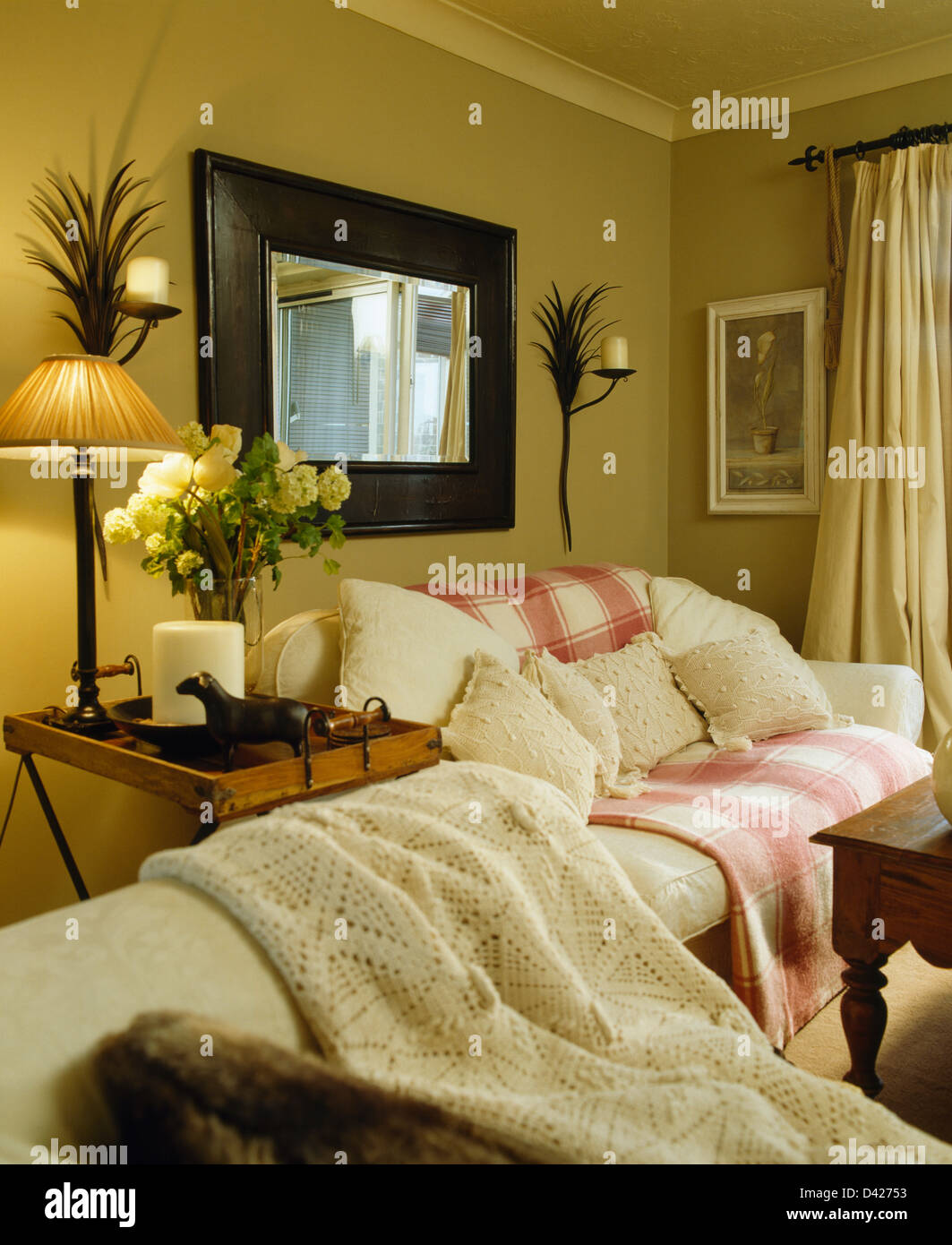 Grande specchio sopra la crema divano con rosa bianca+buttare in ocra  stanza vivente con metallo palm appliques e lampada accesa sul tavolo Foto  stock - Alamy