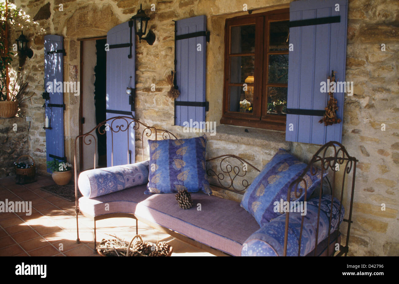 Cuscini blu sul ferro battuto di dormeuse sotto la finestra con persiane blu sulla veranda della casa francese di campagna Foto Stock