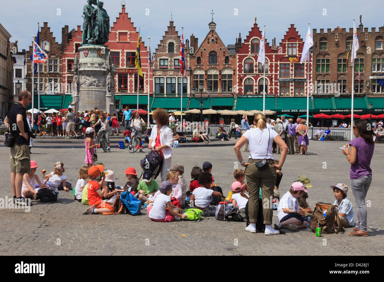 Markt, Bruges, Fiandre Orientali, Belgio. Gruppo di bambini in gita scolastica in seduta il quadrato di mangiare pranzo al sacco Foto Stock