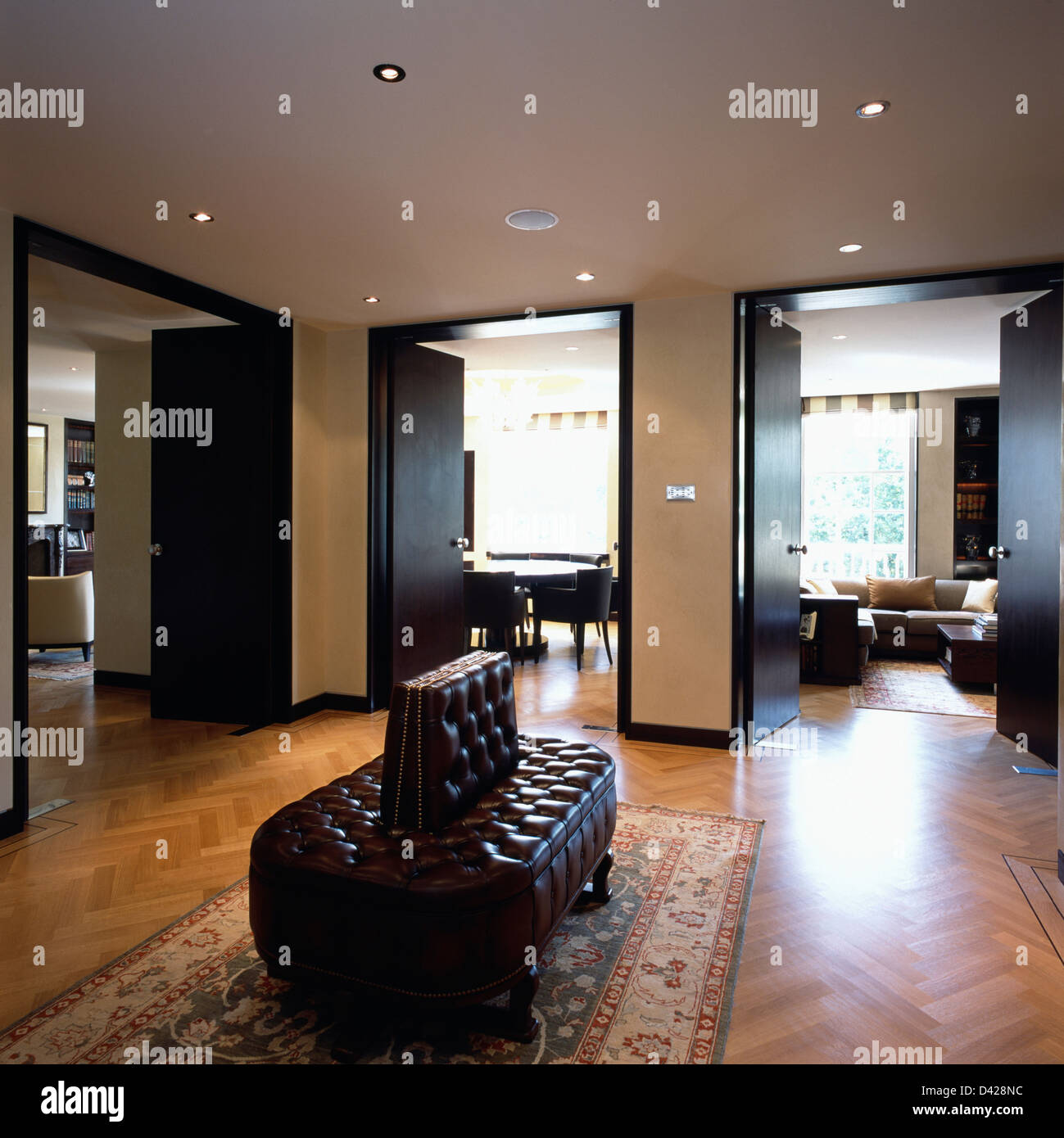 Imbottiti abbottonato sedile in pelle e pavimenti in parquet in appartamento hall con doppie aperte le porte alla sala da pranzo e soggiorno Foto Stock