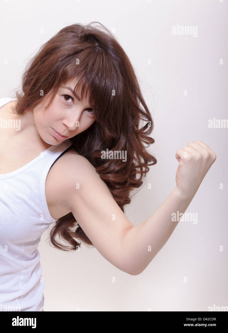 Donna attraente con lunghi mossi brunette capelli inclinato in avanti flettendo il suo braccio e facendo un pugno come guarda la fotocamera Foto Stock