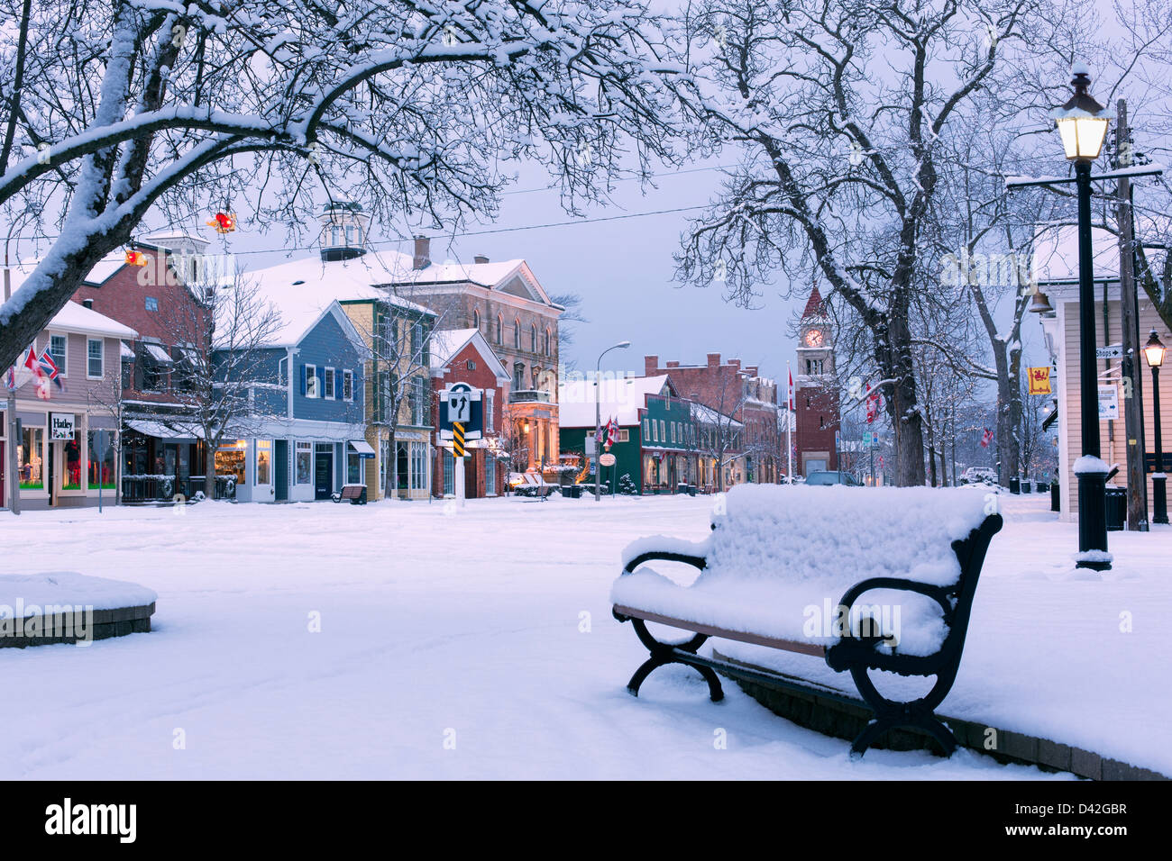 Canada, Ontario, Niagara-on-the-Lake, Queen Street, mattina presto d'inverno, panca parco coperta di neve che mostra una strada principale con negozi. Foto Stock