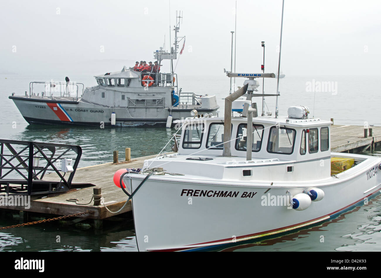 Un guardacoste scivola passato un astice barca legato fino al molo della città su un nebbioso giorno in Bar Harbor, Maine Foto Stock