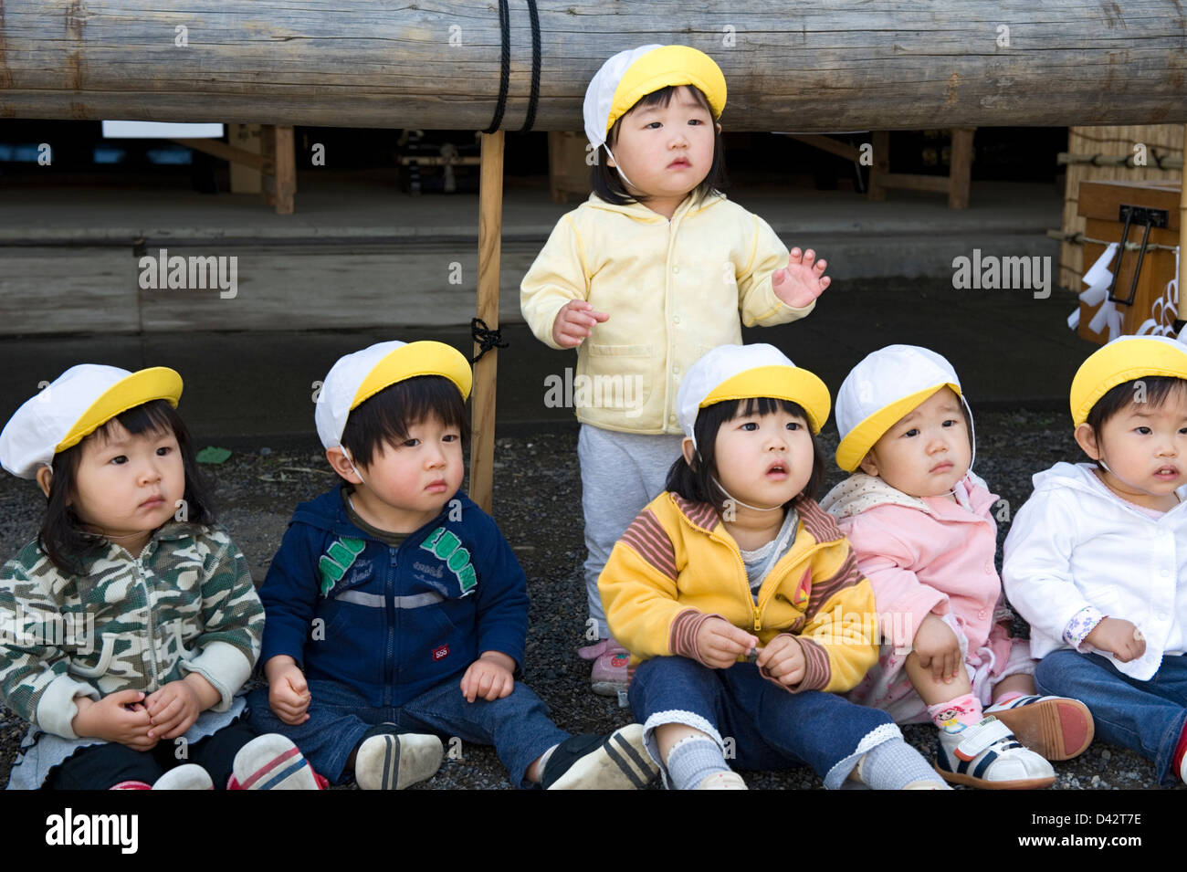 Un gruppo di Giapponesi i bimbi seduti a terra indossando tappi corrispondenti alla ricerca di qualcosa di interessante. Foto Stock