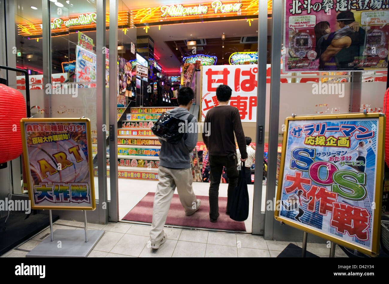Due patroni immettendo un luminose pachinko (flipper) e (slot machine) salone di gioco d'azzardo in Okachimachi, Tokyo. Foto Stock