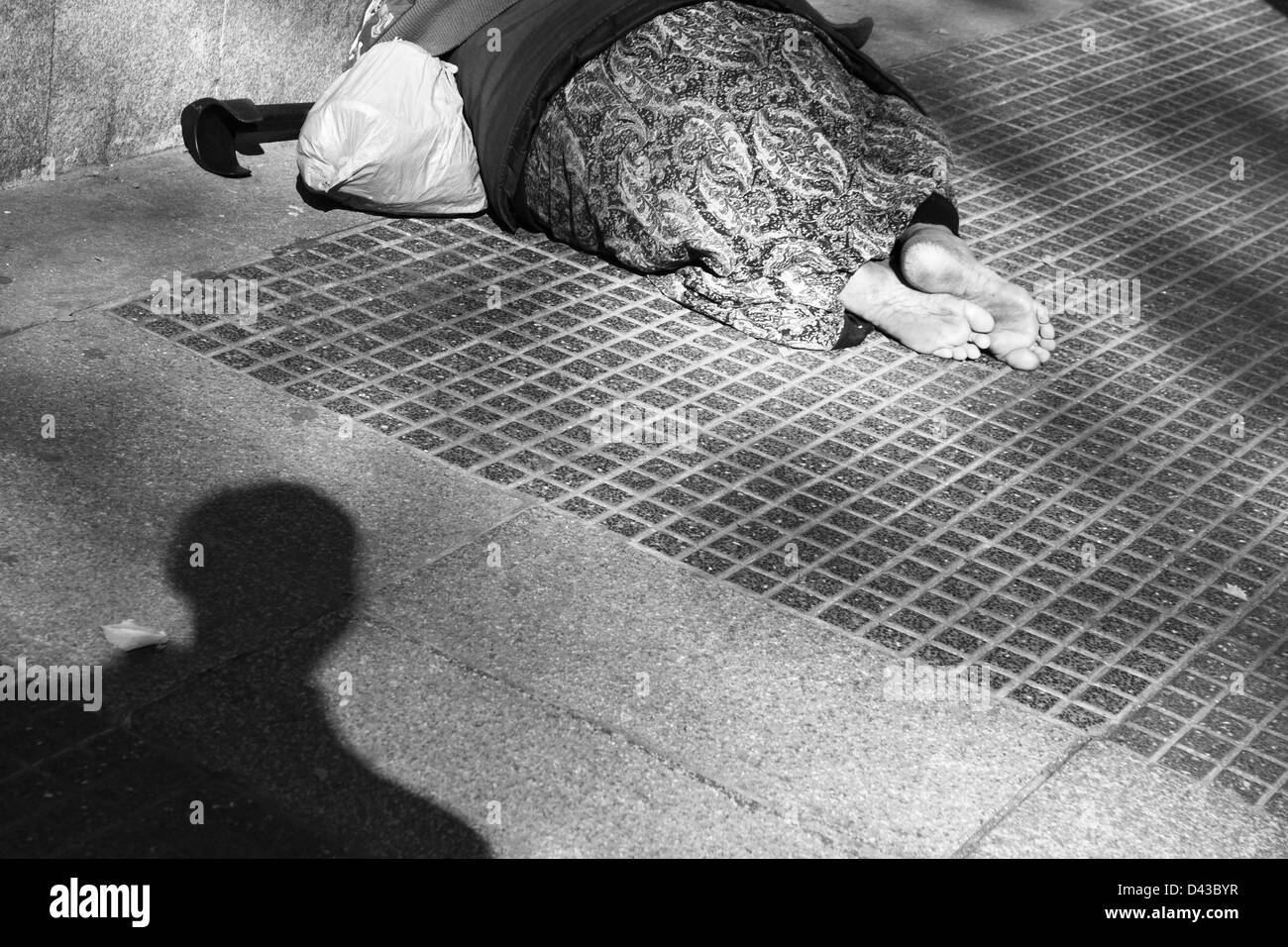 Donna senzatetto senza scarpe sul marciapiede con ombra di passerby Foto Stock