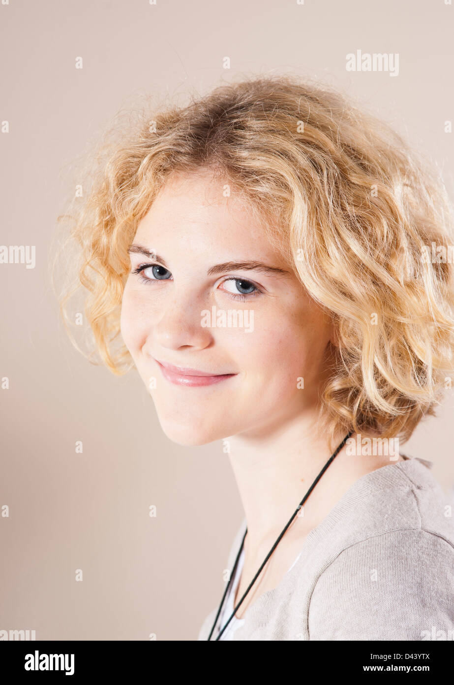 Close-up verticale del Biondo, ragazza con i capelli ricci, sorridente alla fotocamera, Studio shot su sfondo bianco Foto Stock