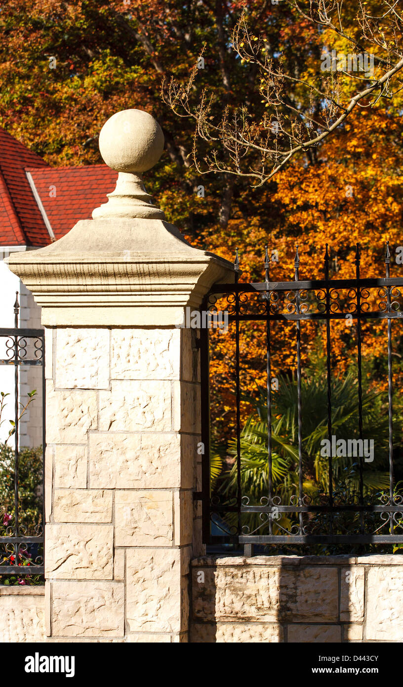 Un decorativi in pietra colonna su un nero ferro battuto recinto intorno ad un estate in autunno Foto Stock